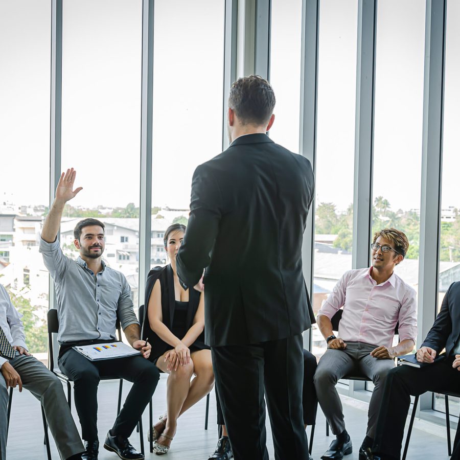 Head of Business Training Sales and Marketing Teams.Male employee raising his hand to ask boss.Many people sat and listened to seminar.